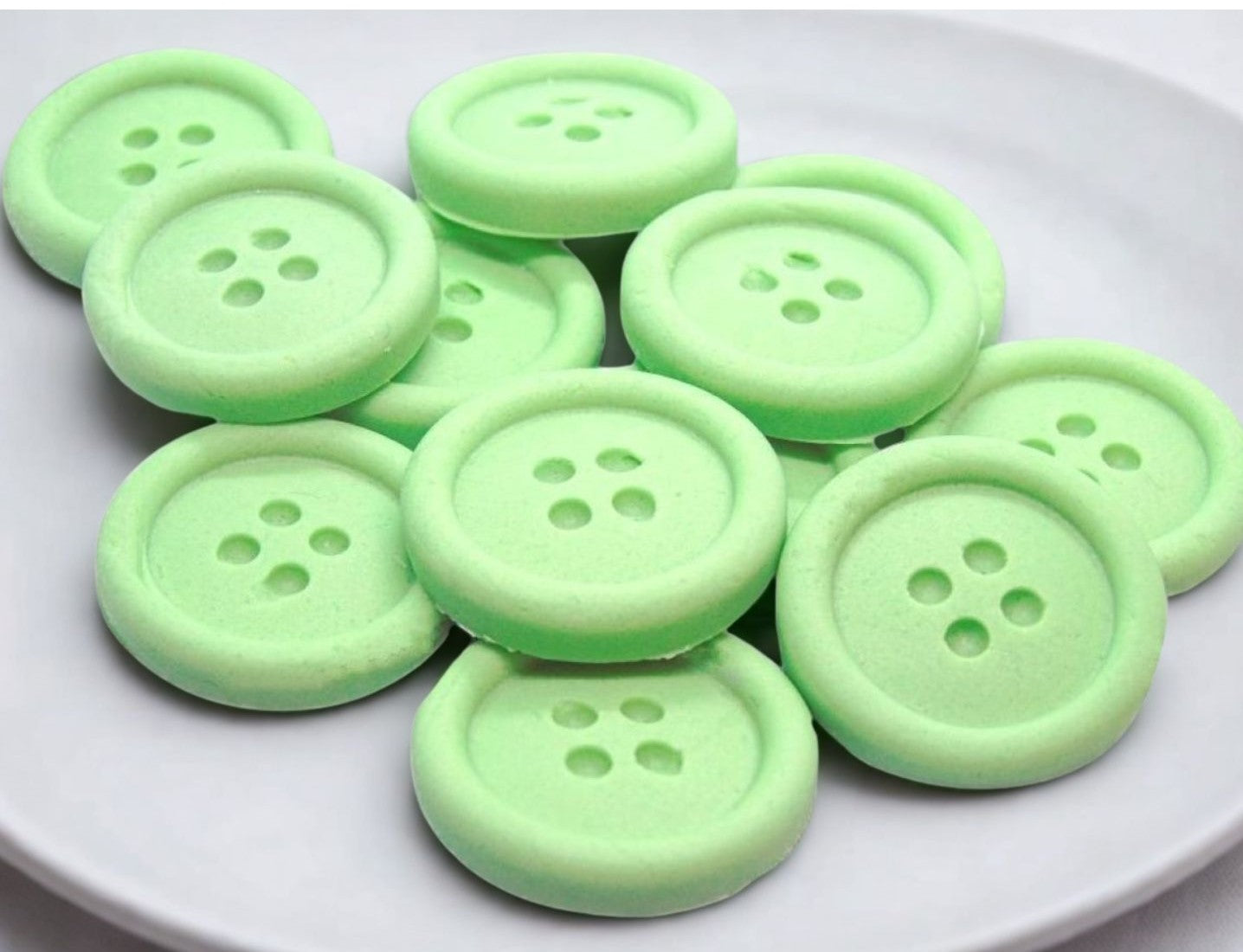 Green edible buttons on a white plate with a white cloth background