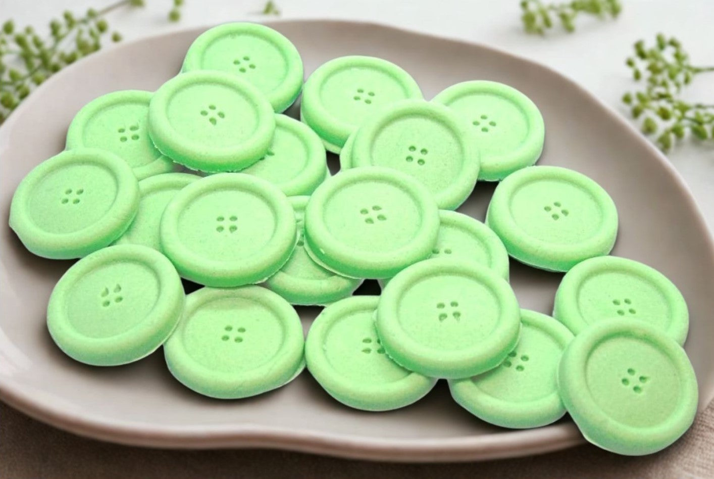 Green coloured edible buttons for baked goods decorations shown in a white dish with a white cloth in the background