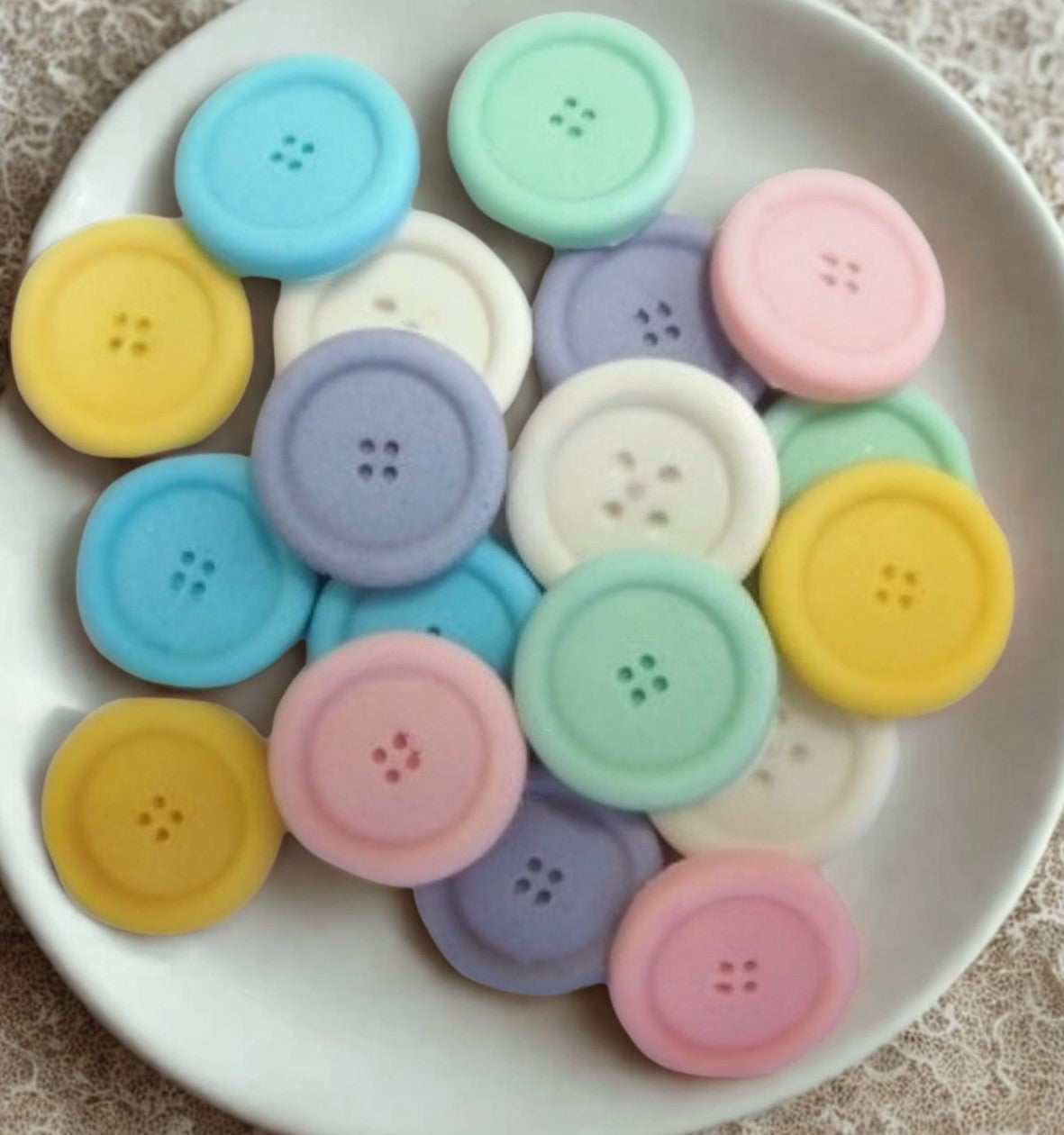 mixed coloured edible buttons for baked goods decorations shown in a white dish with a white cloth in the background