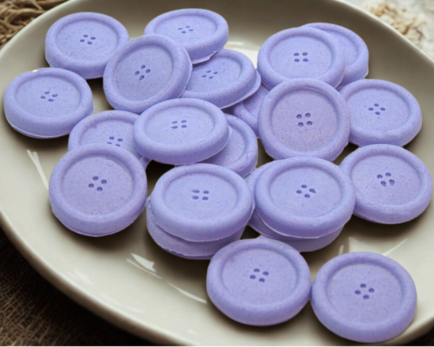Purple coloured edible buttons for baked goods decorations shown in a white dish with a white cloth in the background