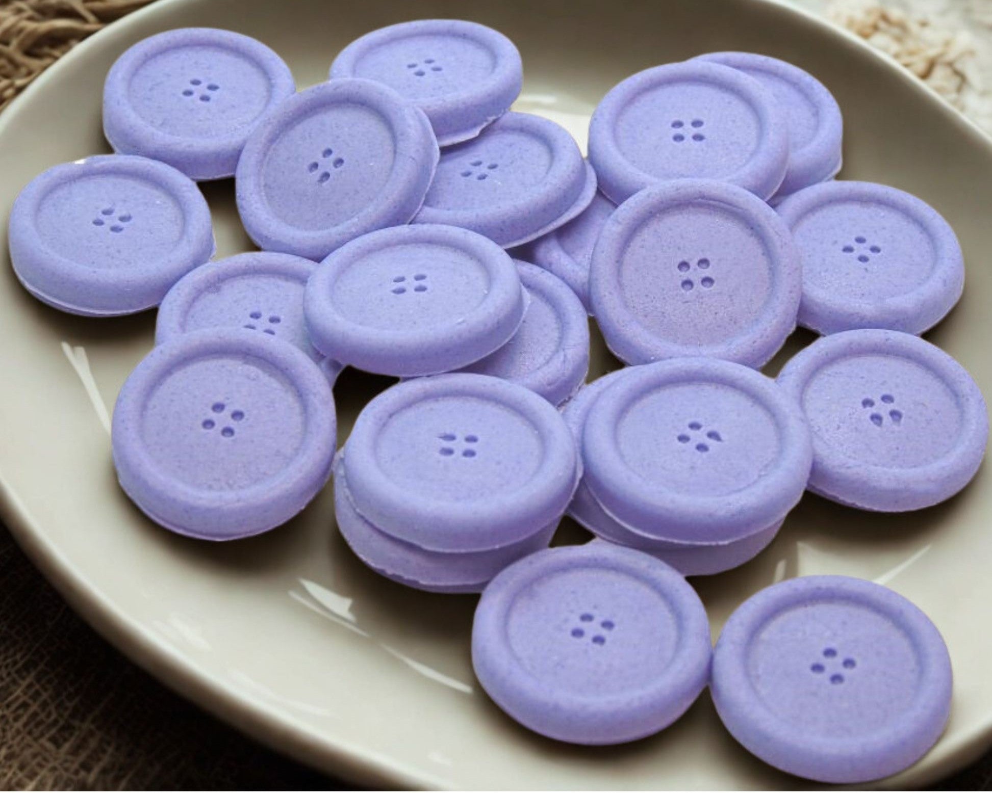 Purple coloured edible buttons for baked goods decorations shown in a white dish with a white cloth in the background