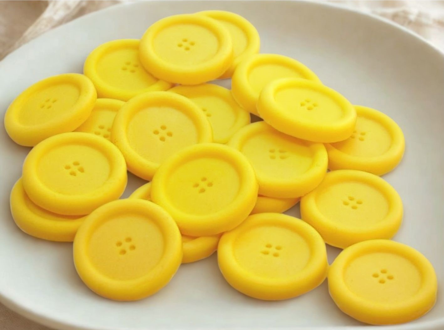 Yellow coloured edible buttons for baked goods decorations shown in a white dish with a white cloth in the background