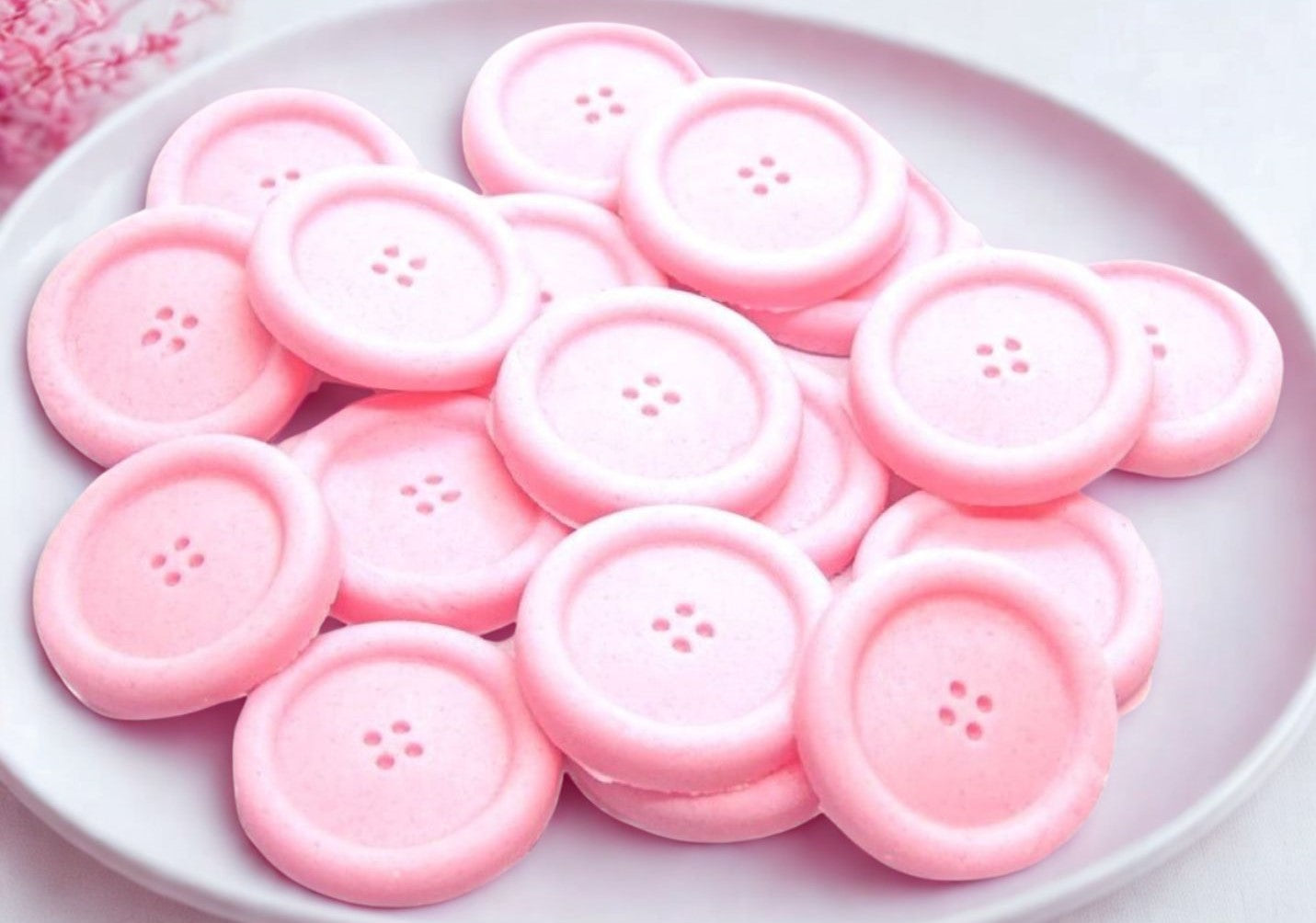 Pink coloured edible buttons for baked goods decorations shown in a white dish with a pink cloth in the background