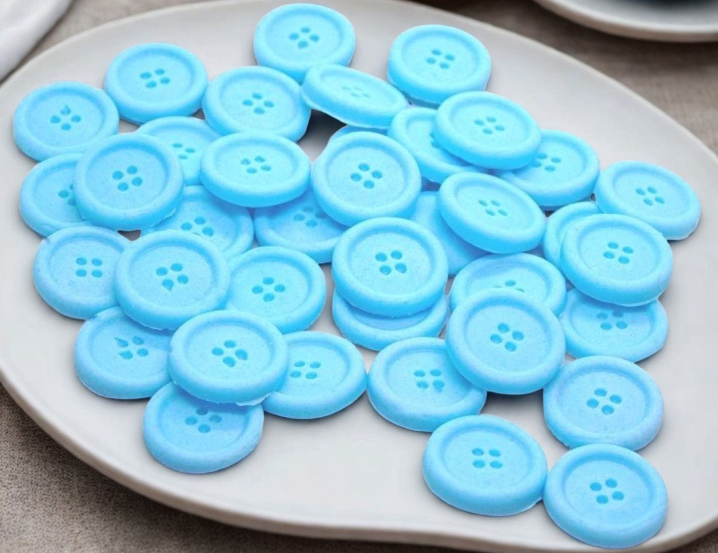 30 blue edible buttons on a white plate against a textured gray background