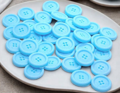 30 blue edible buttons on a white plate against a textured gray background