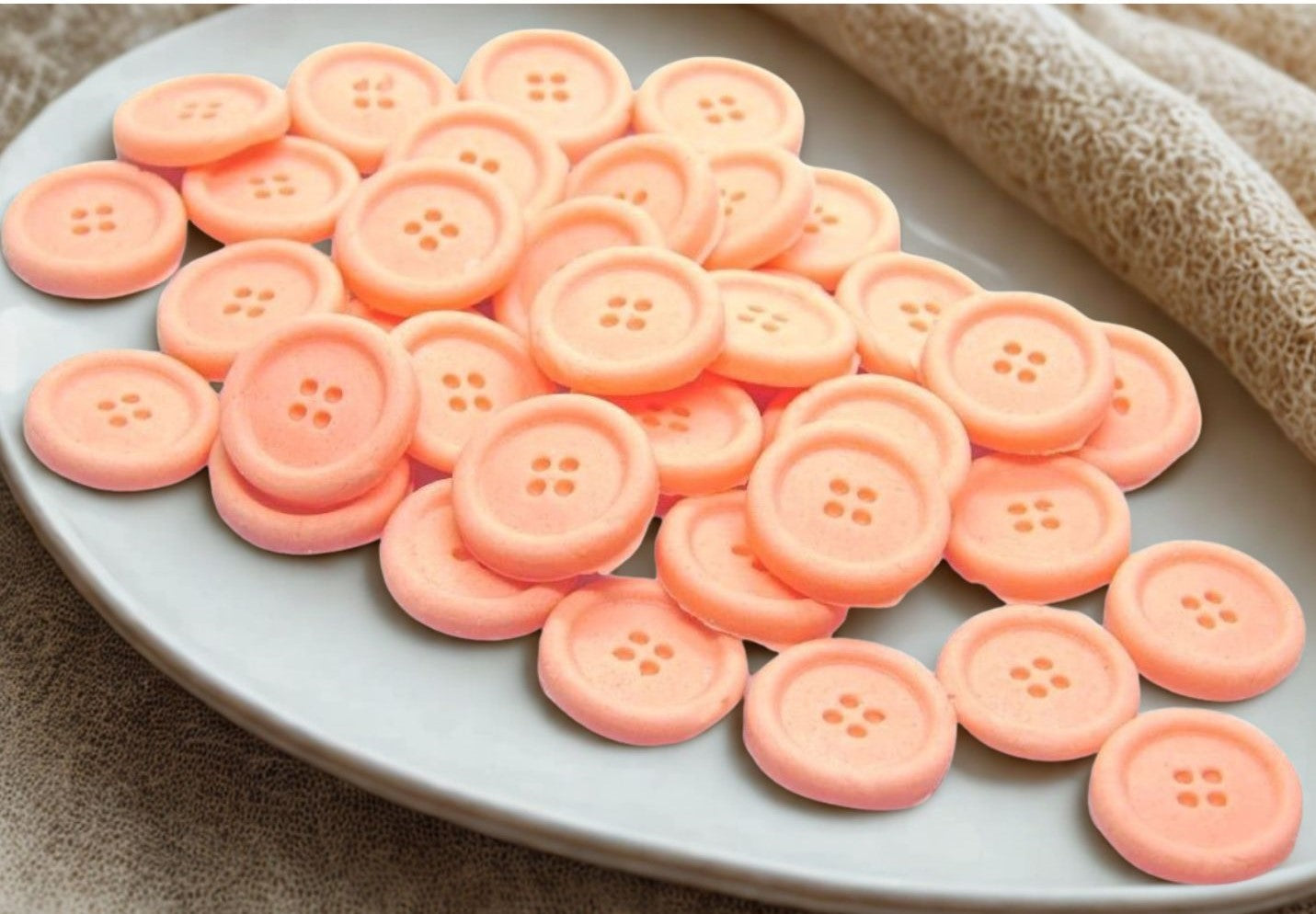 Peach edible buttons on a white plate with a  cloth in the background