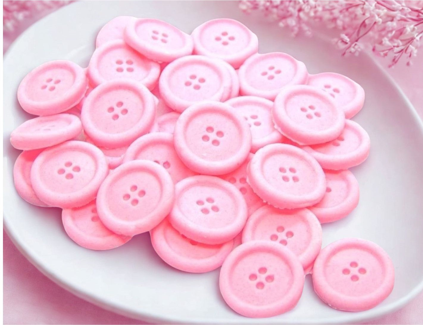 pink edible buttons on a white plate with apink cloth in the background