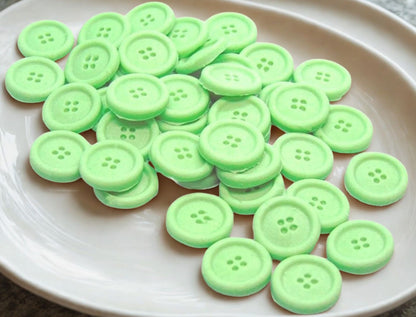 Green edible buttons on a white plate with a white cloth in the background