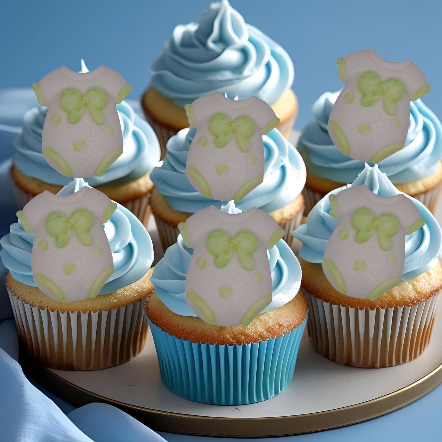 Cupcakes with blue frosting and edible green baby onesie decorations on a plate.
