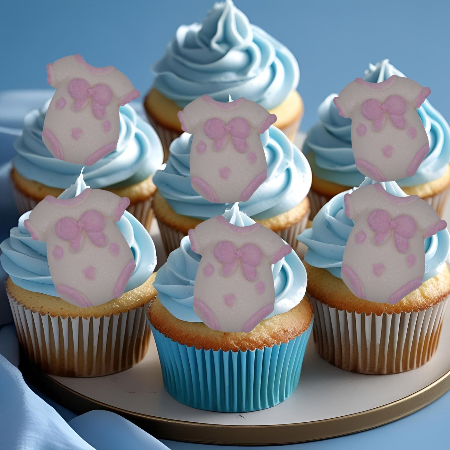 Cupcakes with blue frosting and edible Pink baby vests for baby-themed party decorations on a plate.