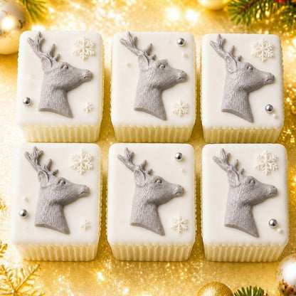 Six square white frosted treats arranged in a 2x3 grid on a shiny gold background, each topped with a gray deer head, white snowflakes, and small silver dots.