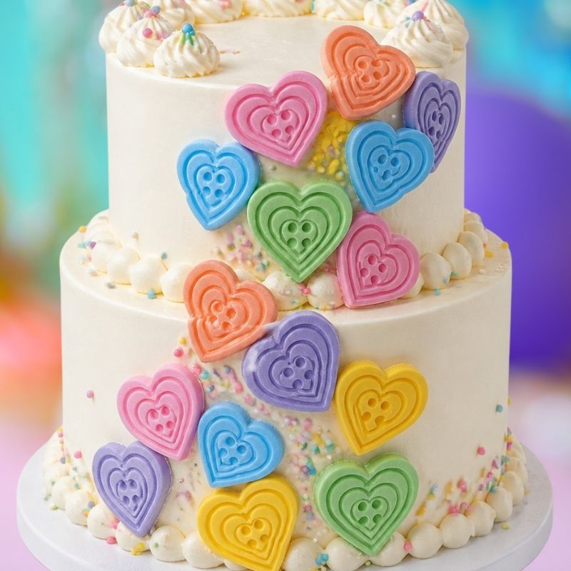 Colorful heart-shaped butto on a two-tiered cake with a blurred colorful backgrounds