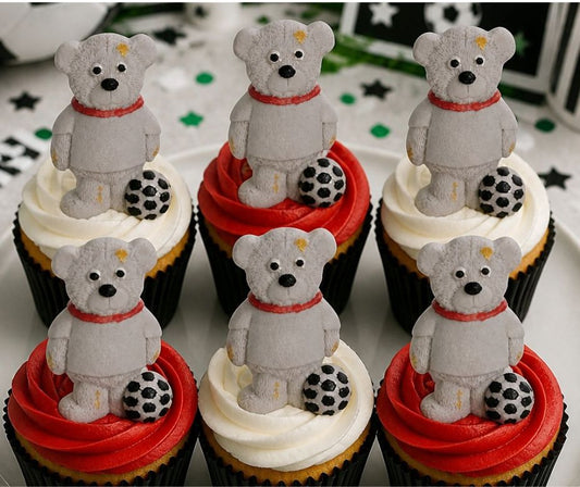 Six decorated cupcakes arranged in two rows, each topped with a small gray teddy bear figurine wearing a red collar and accompanied by a black-and-white football topper. The cupcakes are frosted in alternating white and red swirls, set on a white plate with a star-patterned background.