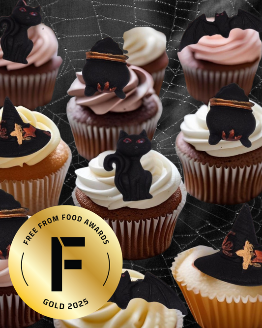 Cupcakes with black cat, cauldron and witches hat decorations on a spider web background, featuring the Free From Food Awards gold 2025 badge.