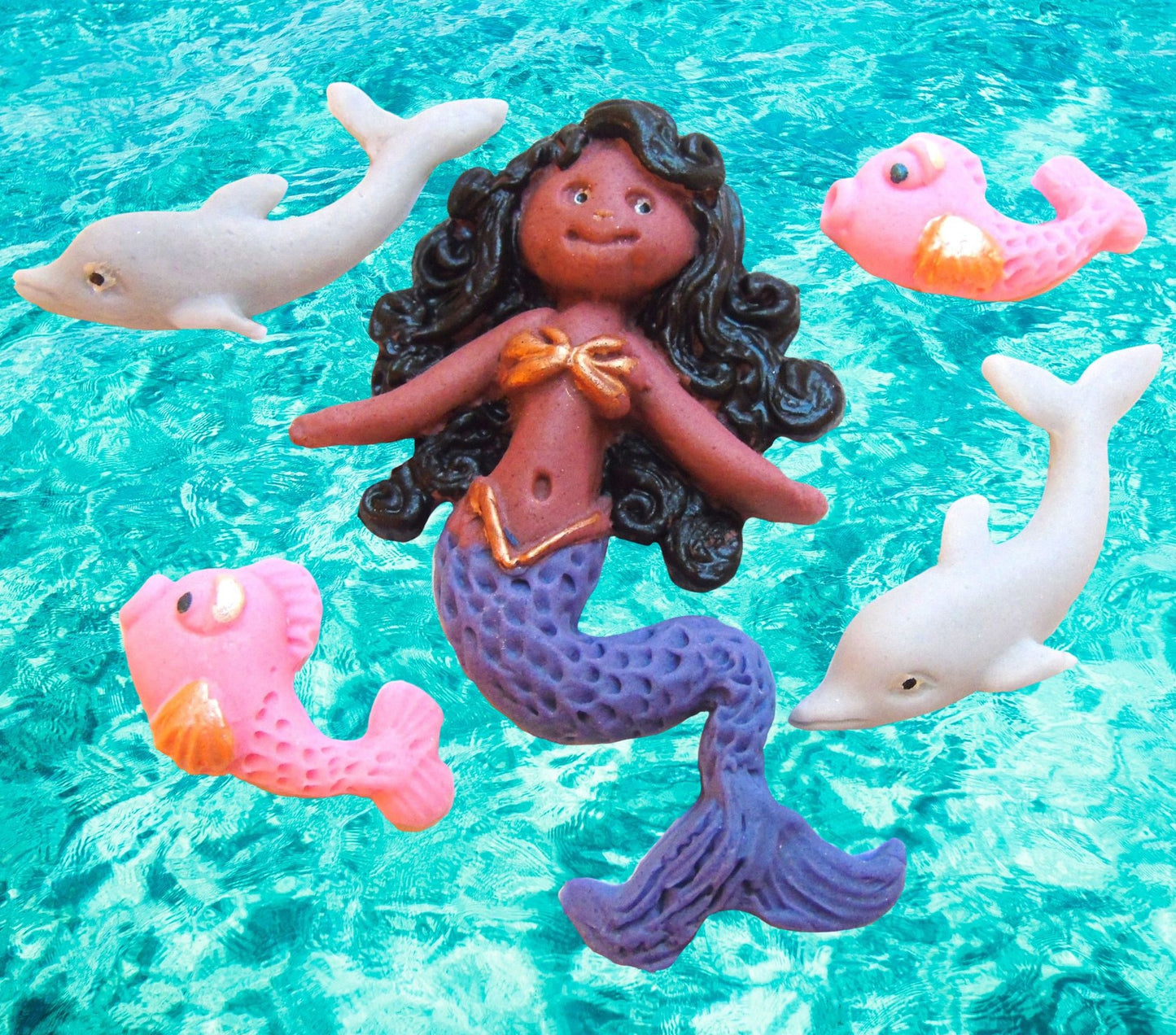 mermaid figurine with dolphins  and fish cake topper decorations on a blue water background 
