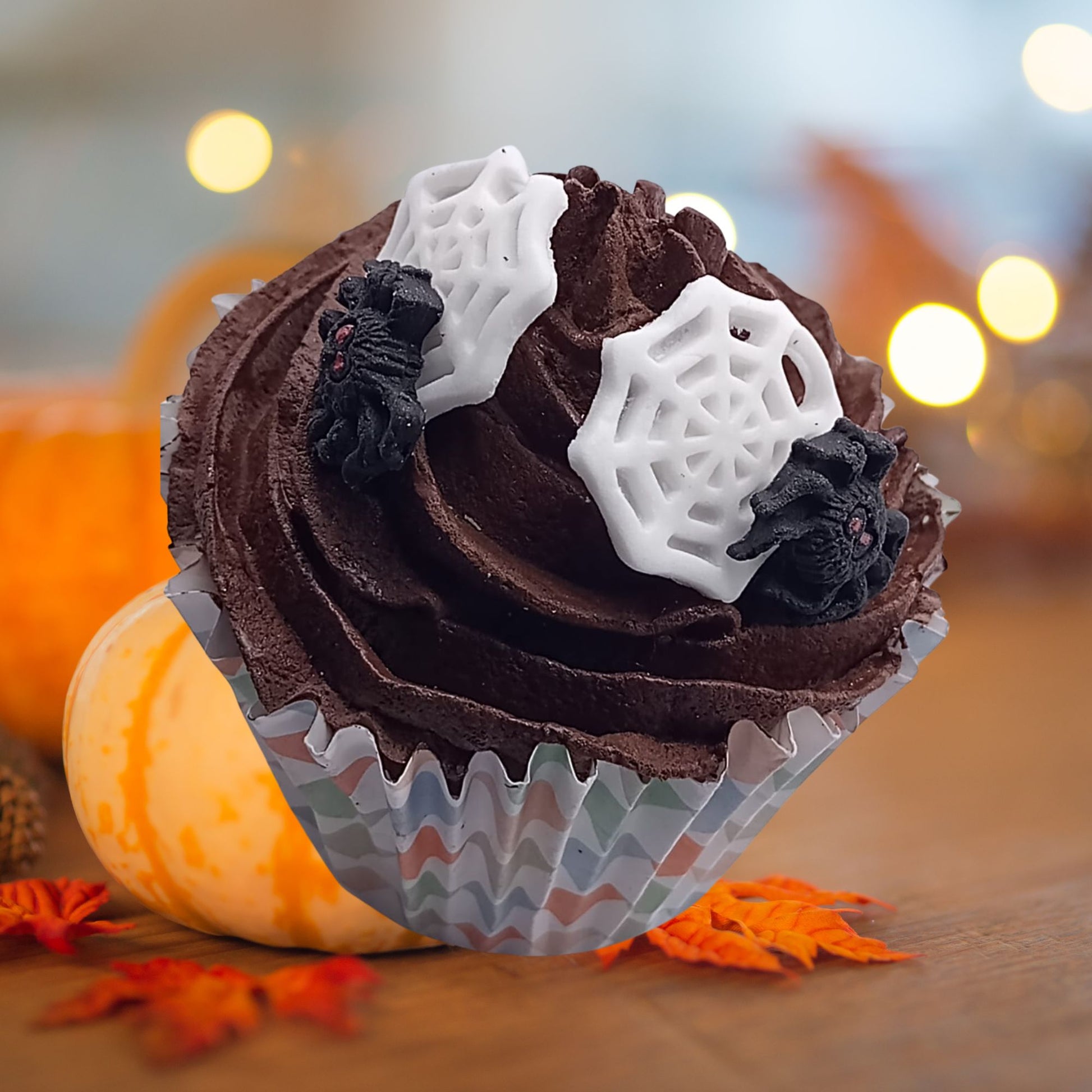 Chocolate cupcake with spiderweb edible decorations on a blurred Halloween-themed background
