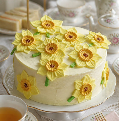 Decorative cake with yellow flower designs on a table setting with tea cups and pastries.