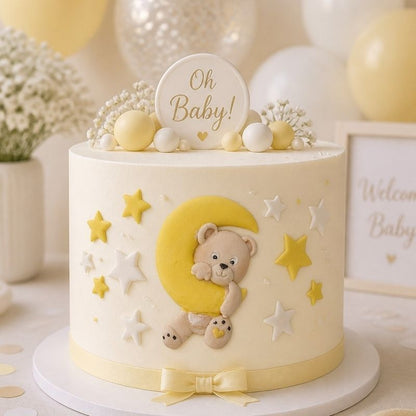 A round baby shower cake decorated with a cream-colored frosting base, featuring a yellow crescent moon, teddy bear, stars, and a small sign that reads 'Oh Baby!' on top.