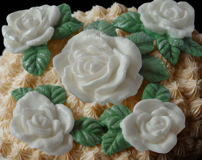 Decorative cake with white roses and green leaves on a textured surface